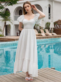 Woman in a white puff sleeve maxi dress with a smocked waist touching her hair by a pool.