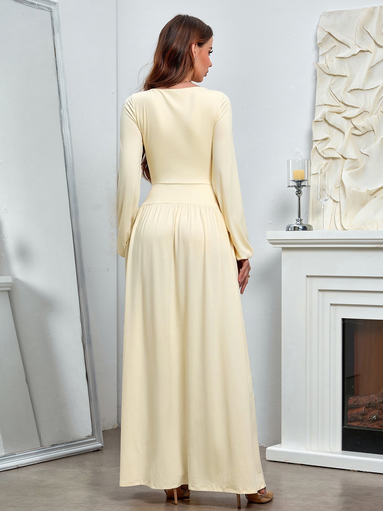 Back view of a woman in a long-sleeved, pale yellow maxi dress with a square neckline.