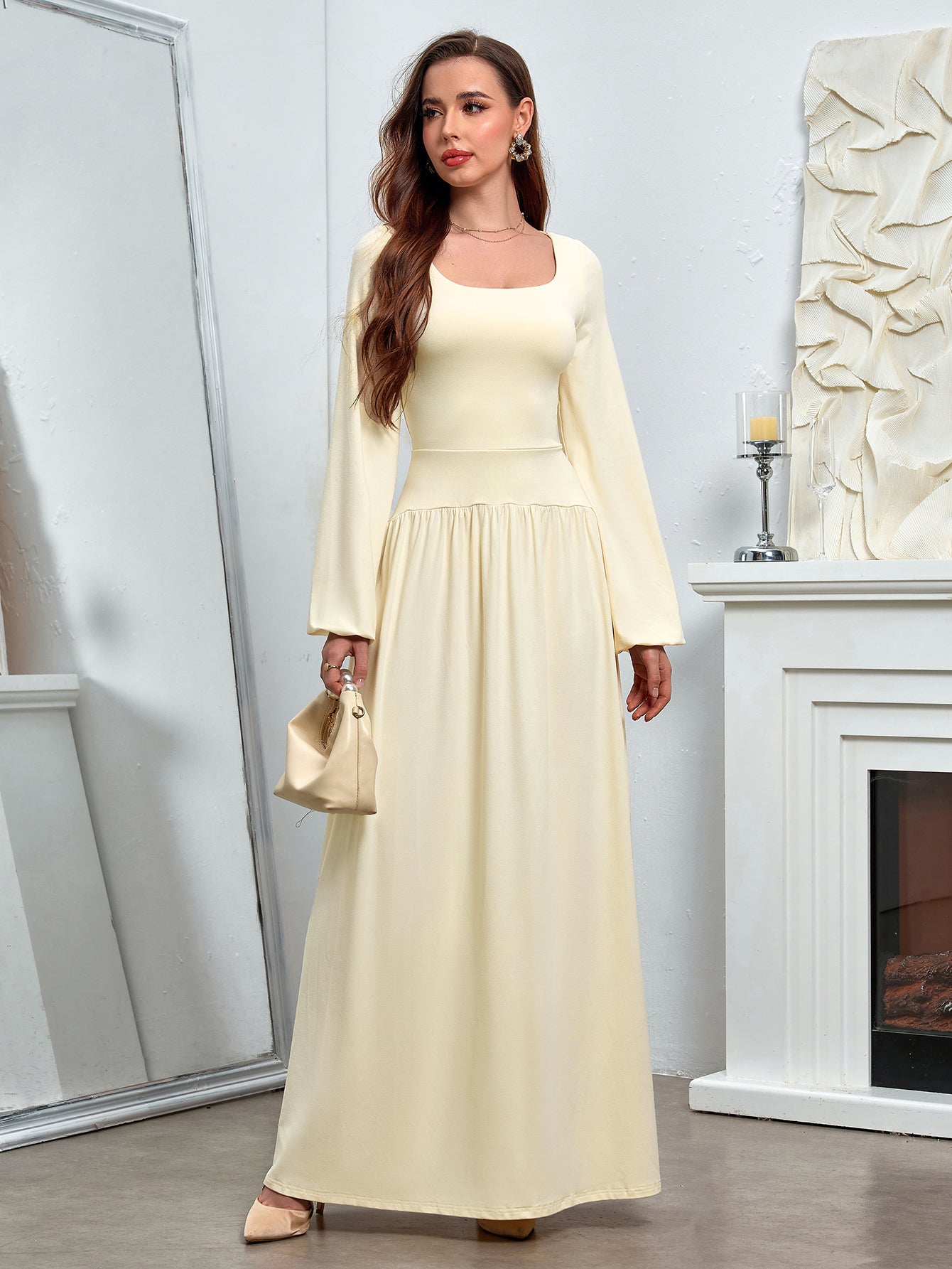Woman in a pale yellow maxi dress with a square neckline and long sleeves, holding a handbag.