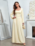 Woman in a pale yellow maxi dress with a square neckline and long sleeves, posing with a handbag.