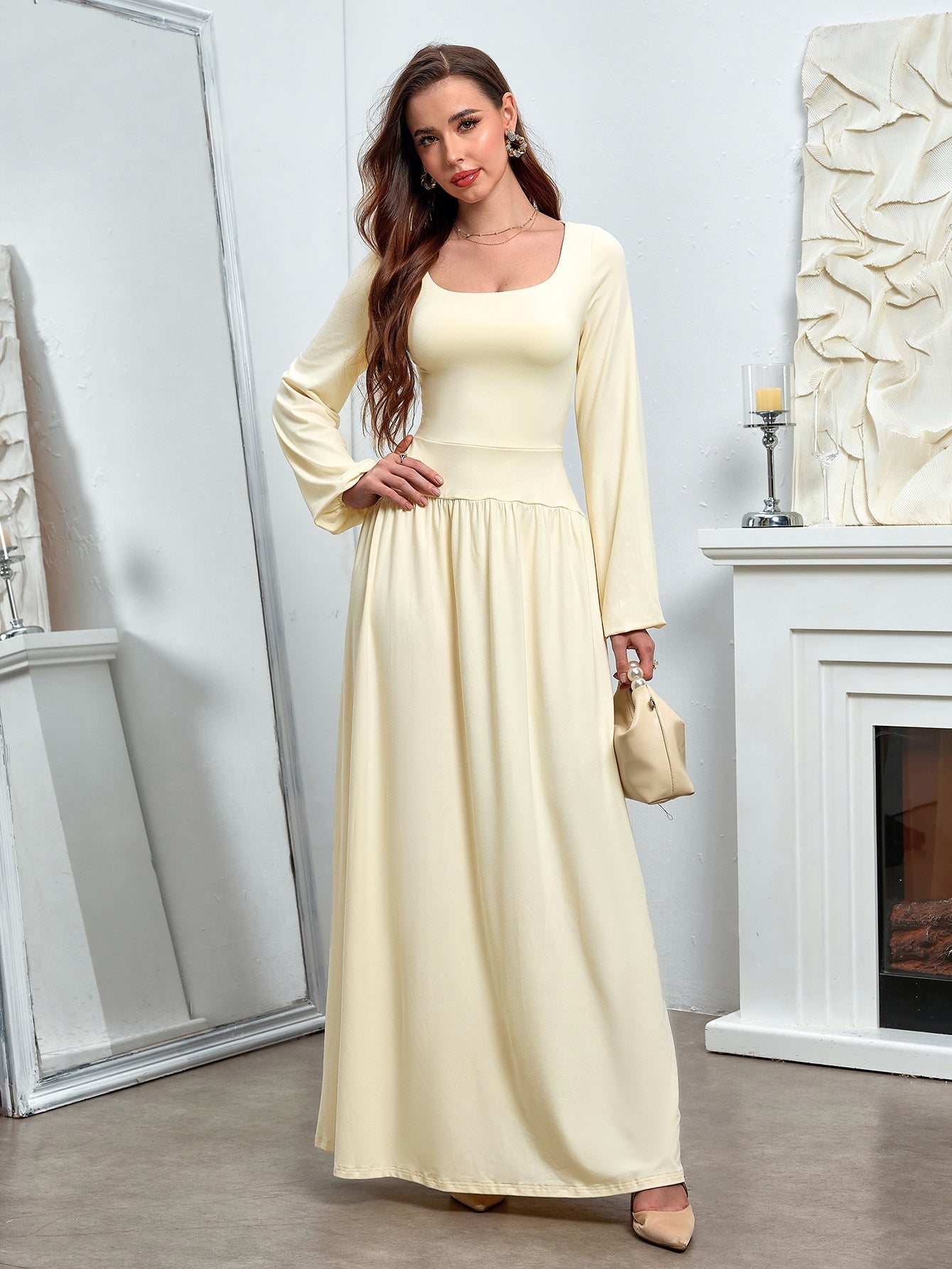 Woman in a pale yellow maxi dress with a square neckline and long sleeves, posing with a handbag.