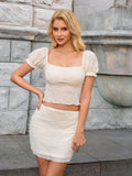 Front view of a woman in a white textured puff sleeve cropped top and matching mini skirt
