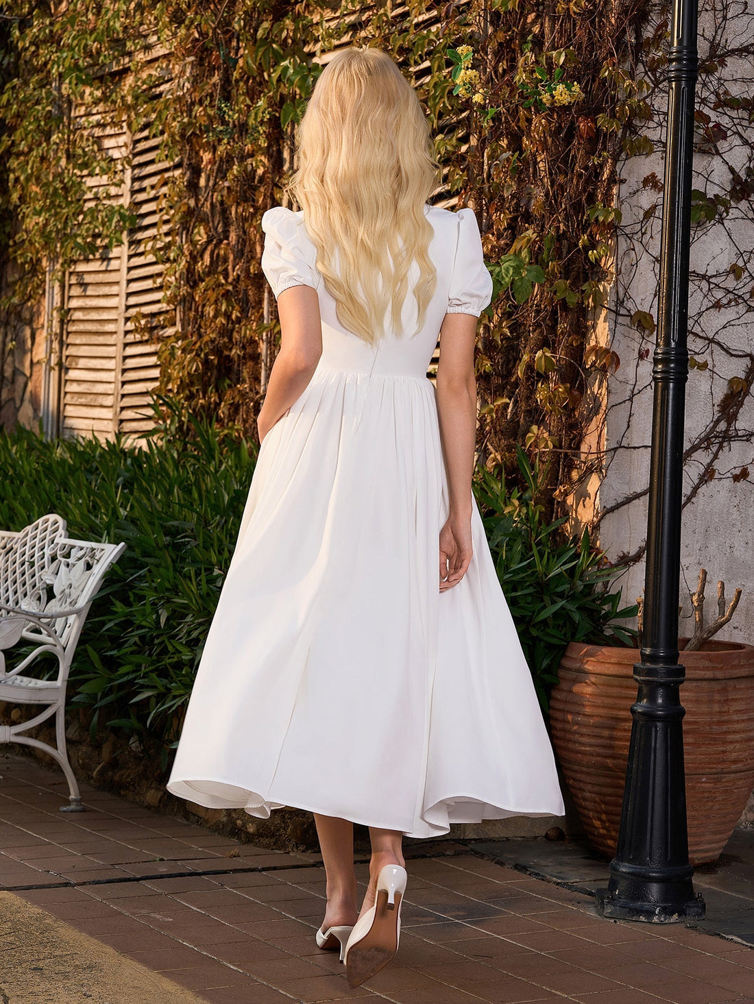 Woman wearing a white midi dress with puff sleeves and a cinched waist, standing outdoors.