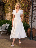 Woman standing with hands in pockets of a white midi dress with puff sleeves.