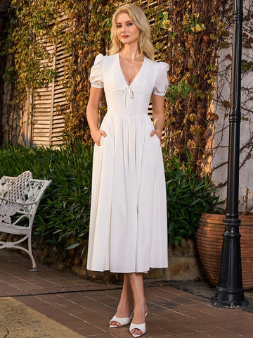 Woman wearing a white midi dress with puff sleeves and a cinched waist, standing outdoors.