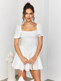 Woman holding a white handbag and wearing a white short dress with puff sleeves and a square neckline