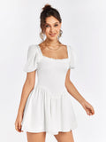 Woman smiling and wearing a white short dress with puff sleeves and a square neckline