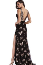 Back view of a woman in a black sequined V-neck, sleeveless evening gown with a high leg slit and open back.