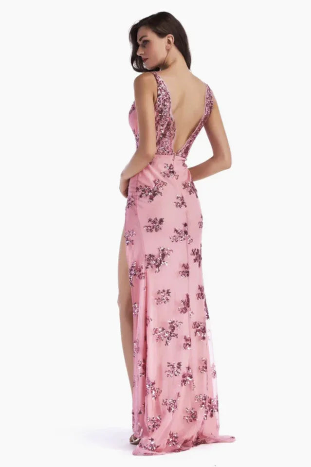 Back view of a woman in a pink sequined V-neck, sleeveless evening gown with a high leg slit and open back.