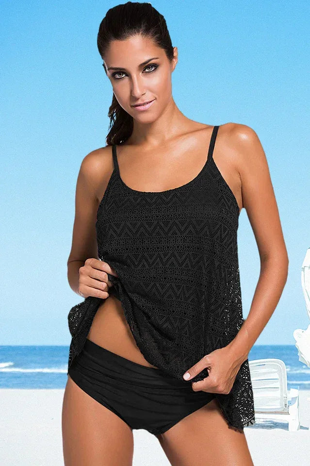 Woman wearing a black crochet overlay tankini top and matching high-waisted bikini bottom on a beach.