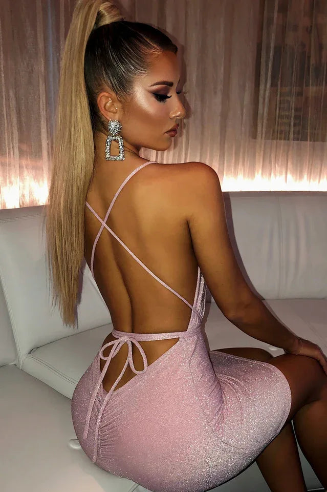 Woman in a champagne sparkly bodycon mini dress with spaghetti straps and a backless tie-back detail, viewed from the side.