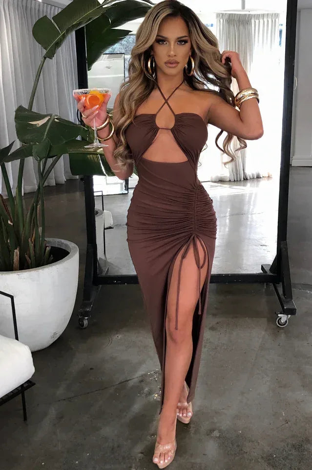 Woman holding a cocktail in a brown halter neck ruched maxi dress with a high slit.