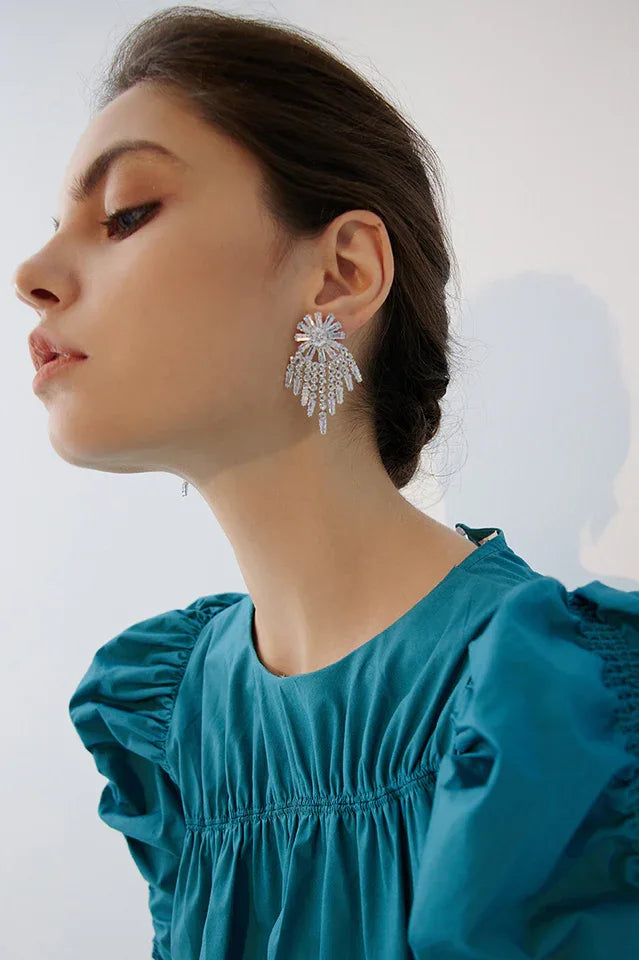 Woman wearing sparkling dangle earrings with a floral-inspired top and tiered fringe design. Main image