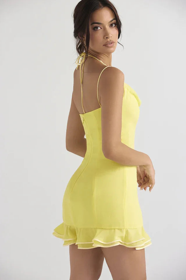 Side view of a woman in a yellow satin mini dress with a halter tie back and ruffle hem.