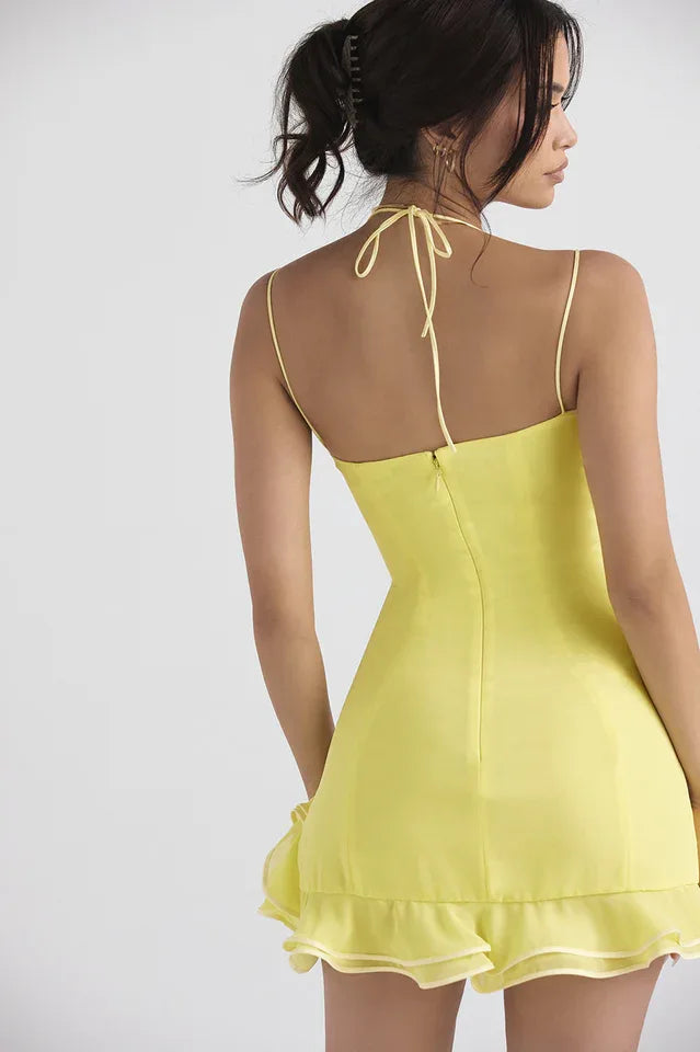Back view of a woman in a yellow satin mini dress showing the halter tie detail and zipper.