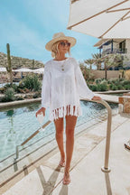 Woman in a white knit tunic with fringe hem standing by a pool