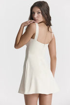 Model wearing a cream white duchess satin mini dress with wide straps and a square neckline, back view showing zipper.