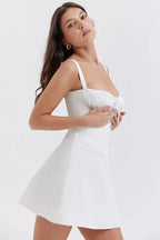 Woman adjusting the tie on the bust of a white ruched mini dress.