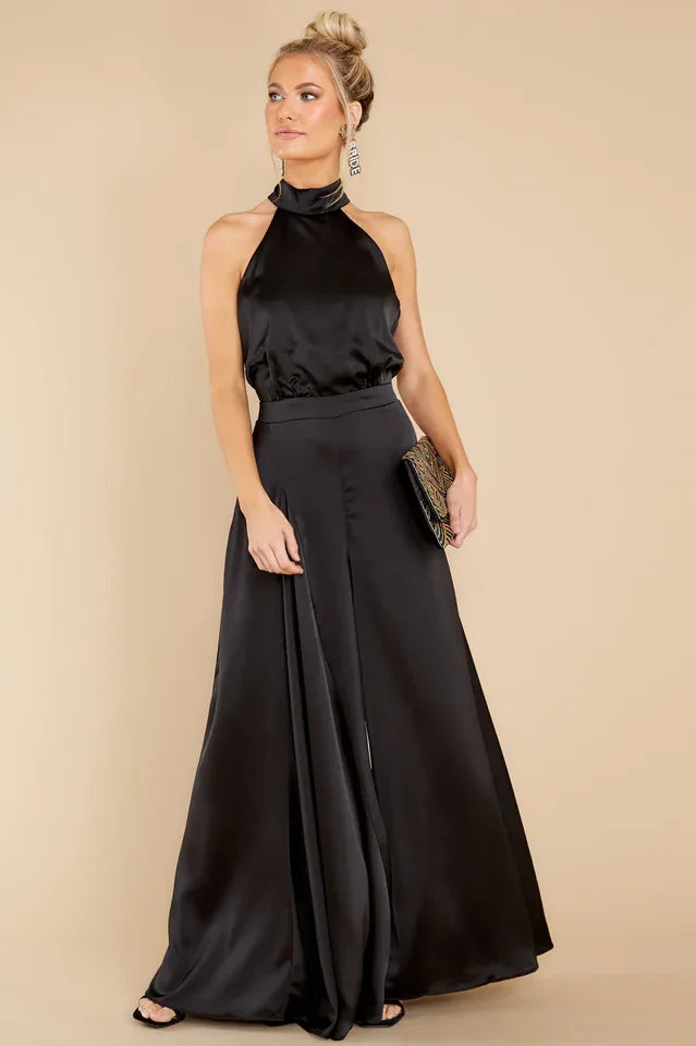 woman wearing a black halter neck satin jumpsuit with wide leg pants, posing with a clutch