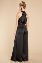 woman wearing a black halter neck satin jumpsuit with wide leg pants and a tie back closure