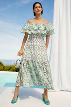 Woman wearing a white and green off-the-shoulder midi dress with ruffle trim and embroidered circular patterns.