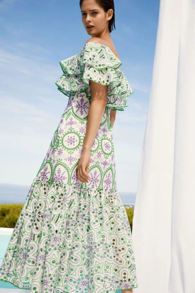 Woman wearing a white and green off-the-shoulder midi dress with ruffle trim and embroidered circular patterns, viewed from the side.