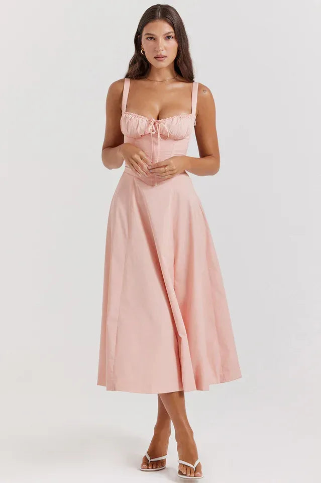 Woman wearing a pink cotton poplin midi dress with a sweetheart neckline, tie front detail, and spaghetti straps.