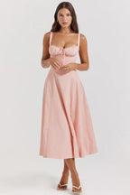 Woman wearing a pink cotton poplin midi dress with a sweetheart neckline, tie front detail, and spaghetti straps.