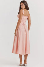 Rear view of a woman in a pink cotton poplin midi dress with a lace-up back detail and a-line skirt.
