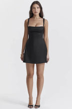 Full body front view of a model in a black satin mini dress with a square neckline.