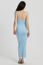 Back view of a woman in a light blue ruched one-shoulder maxi dress with a floral applique