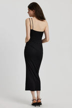 Back view of a woman in a black ruched one-shoulder maxi dress with a floral applique
