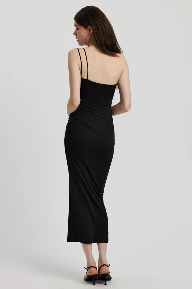 Back view of a woman in a black ruched one-shoulder maxi dress with a floral applique