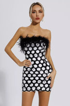 Woman wearing a black and white sequin polka dot mini dress with black feather trim