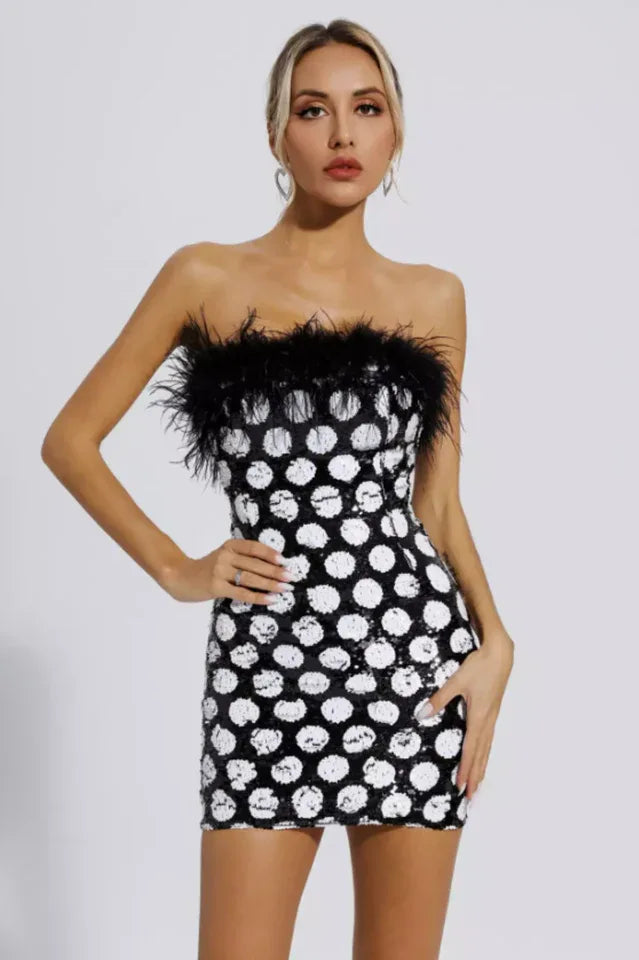 Woman wearing a black and white sequin polka dot mini dress with black feather trim