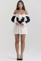 Full length shot of a woman modeling a black and cream off-the-shoulder dress with a bow and flared cuffs.