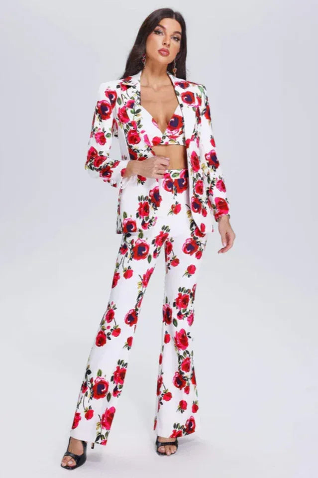 Woman wearing a white blazer and flared trousers with a red floral print, front view.