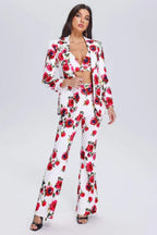 Woman wearing a white blazer and flared trousers with a red floral print, front view.