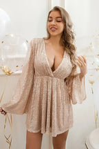 Model in a rose gold sequin party dress with bell sleeves and a deep V-neck, smiling and posing with balloons.