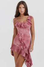 Woman wearing a pink printed mini dress with asymmetrical ruffle hem and spaghetti straps.