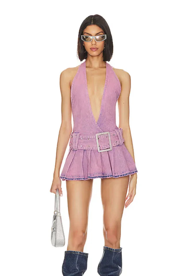 Woman wearing a lavender washed denim halter neck mini dress with a plunging V-neckline, a wide embellished belt, and a pleated skirt, paired with sunglasses and denim boots.