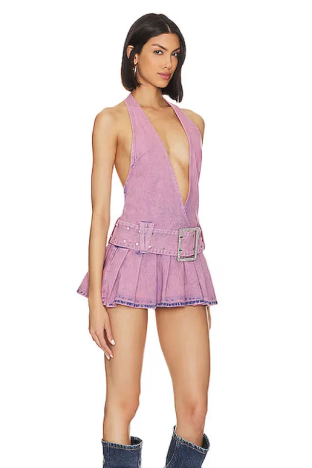 Side view of a woman wearing a lavender washed denim halter neck mini dress with a plunging V-neckline, a wide embellished belt, and a pleated skirt, paired with denim boots.