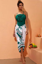Full body shot of a woman in a green swimsuit and sarong.