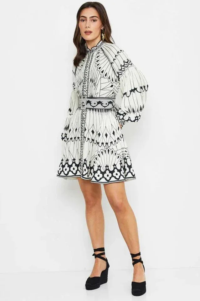 Full body shot of a woman in a cream and black printed mini dress with balloon sleeves and a belt