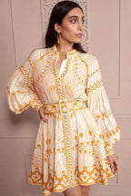 Woman wearing a cream and yellow printed mini dress with balloon sleeves and a belt