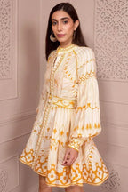 Side view of a woman in a cream and yellow printed mini dress with balloon sleeves and a belt