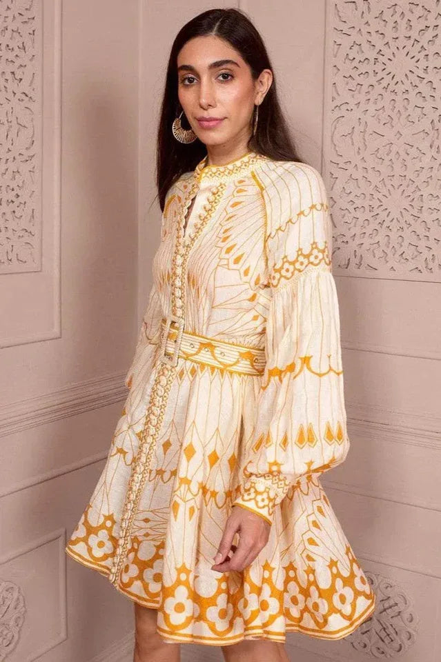 Side view of a woman in a cream and yellow printed mini dress with balloon sleeves and a belt