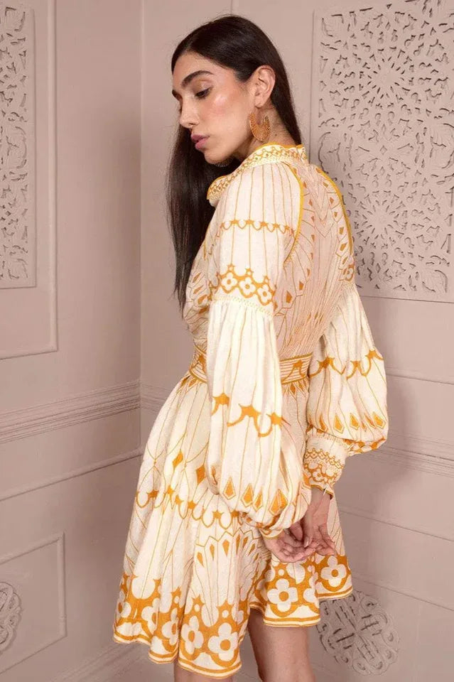 Back view of a woman in a cream and yellow printed mini dress with balloon sleeves and a belt