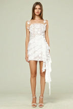 Woman wearing a white lace mini dress with a square neckline and ruffled asymmetrical hem