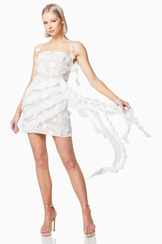 Model posing in a white lace mini dress with a flowing sash